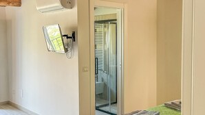 A bedroom with a green quilted bedspread, a wooden ceiling, a wall-mounted air conditioning unit, and a glass door leading to a bathroom. - Dimora San Martino (Monteforte Irpino)