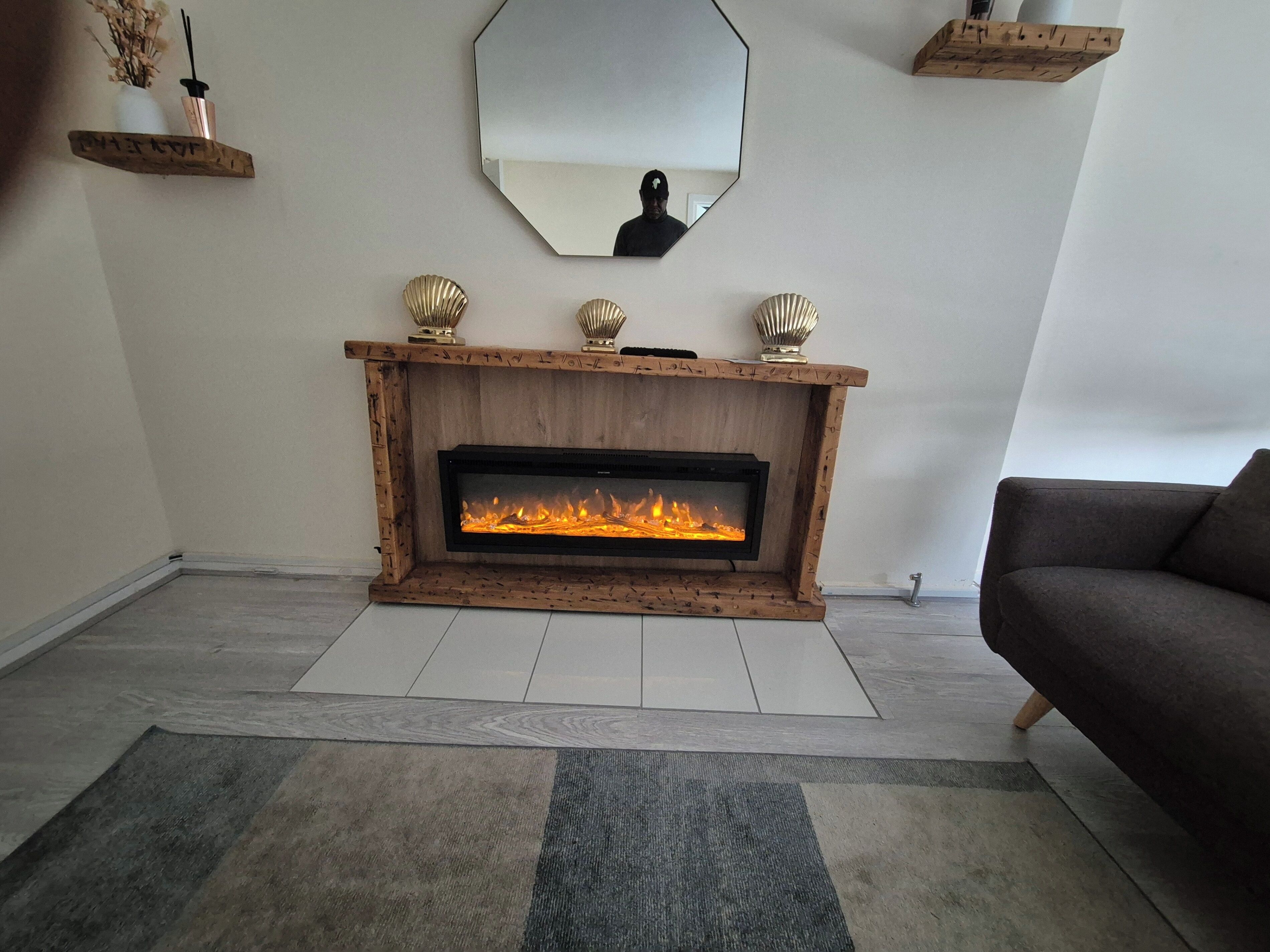 Een moderne woonkamer met een houten open haard, een grote spiegel en decoratieve objecten op zwevende planken.