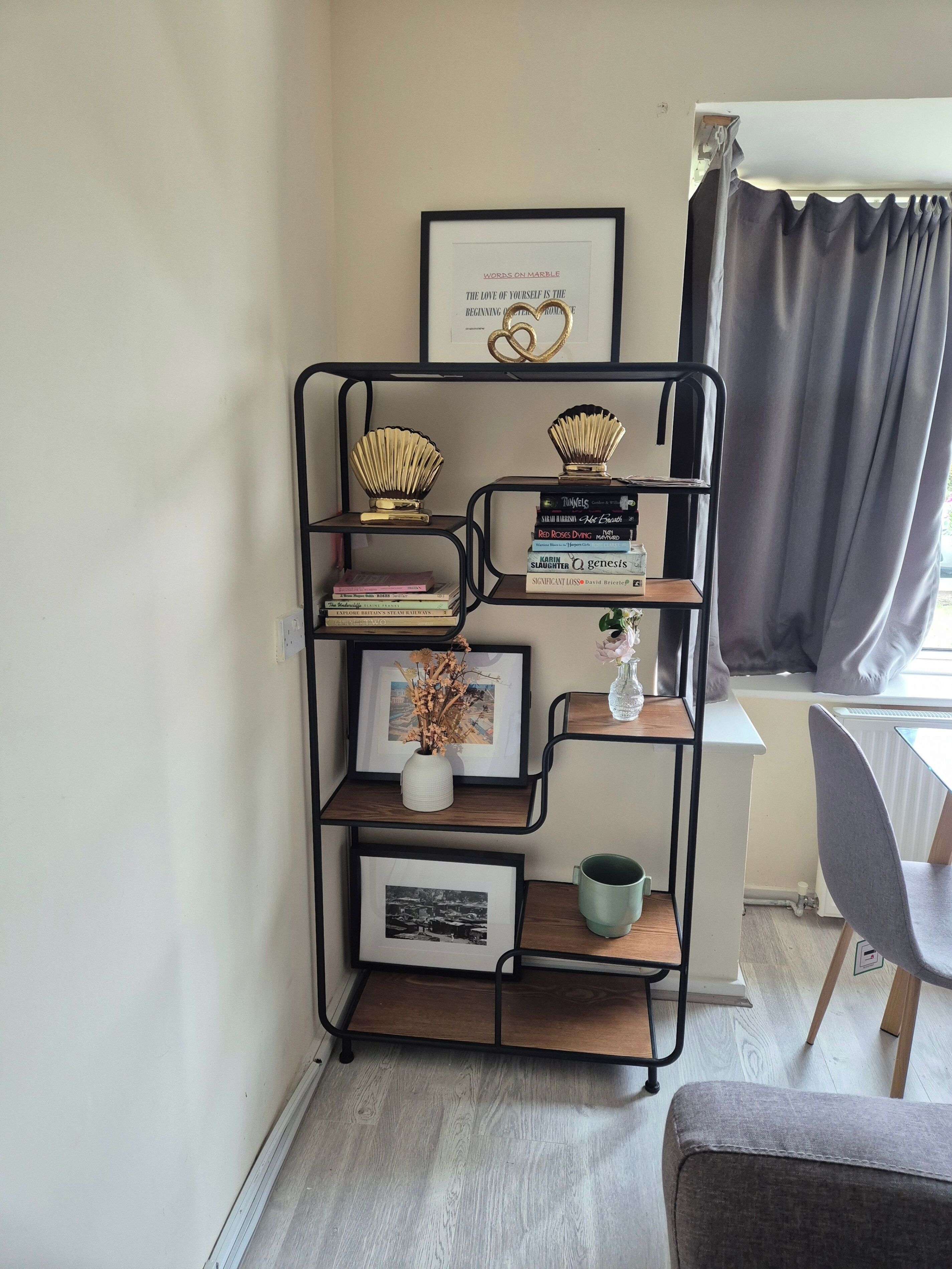 A bookshelf with books and decorative items, a framed quote on the wall, and a window with curtains.