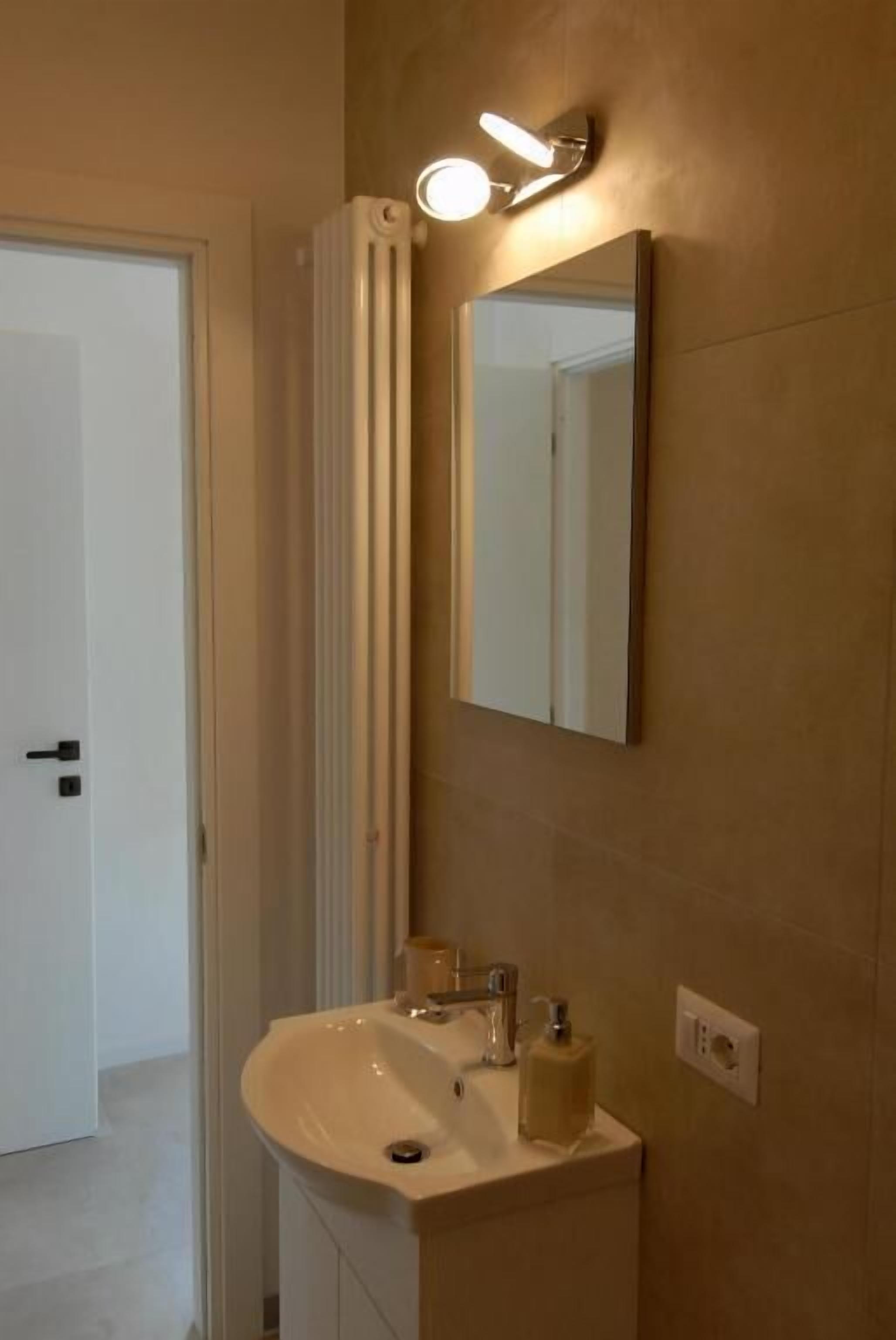 A modern bathroom with a white sink, a mirror, and a light fixture above it.