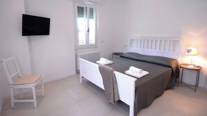 A bedroom with a bed, a chair, a bedside table, a lamp, and a TV mounted on the wall. - Le Case di Elena (Gignese)