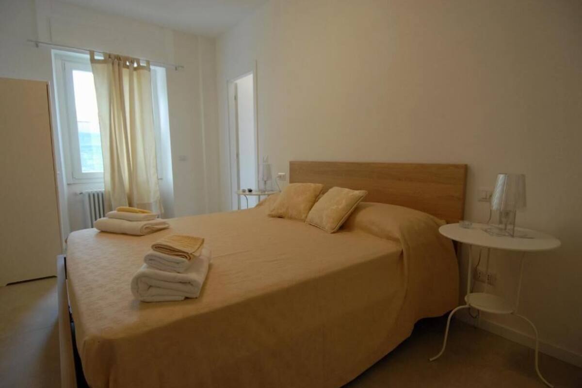A neatly made bed with a wooden headboard, a bedside table with a lamp, and a window with curtains.