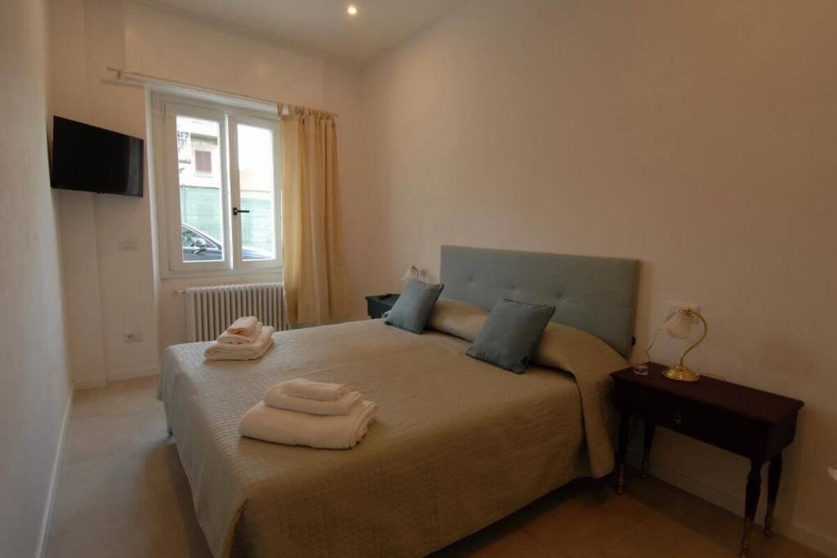 A bedroom with a bed, a nightstand, a TV mounted on the wall, and a window with curtains.