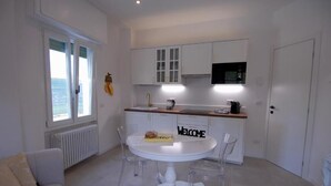 A modern kitchen with white cabinetry, a round dining table, and a view of the sea through large windows. - Le Case di Elena (Gignese)