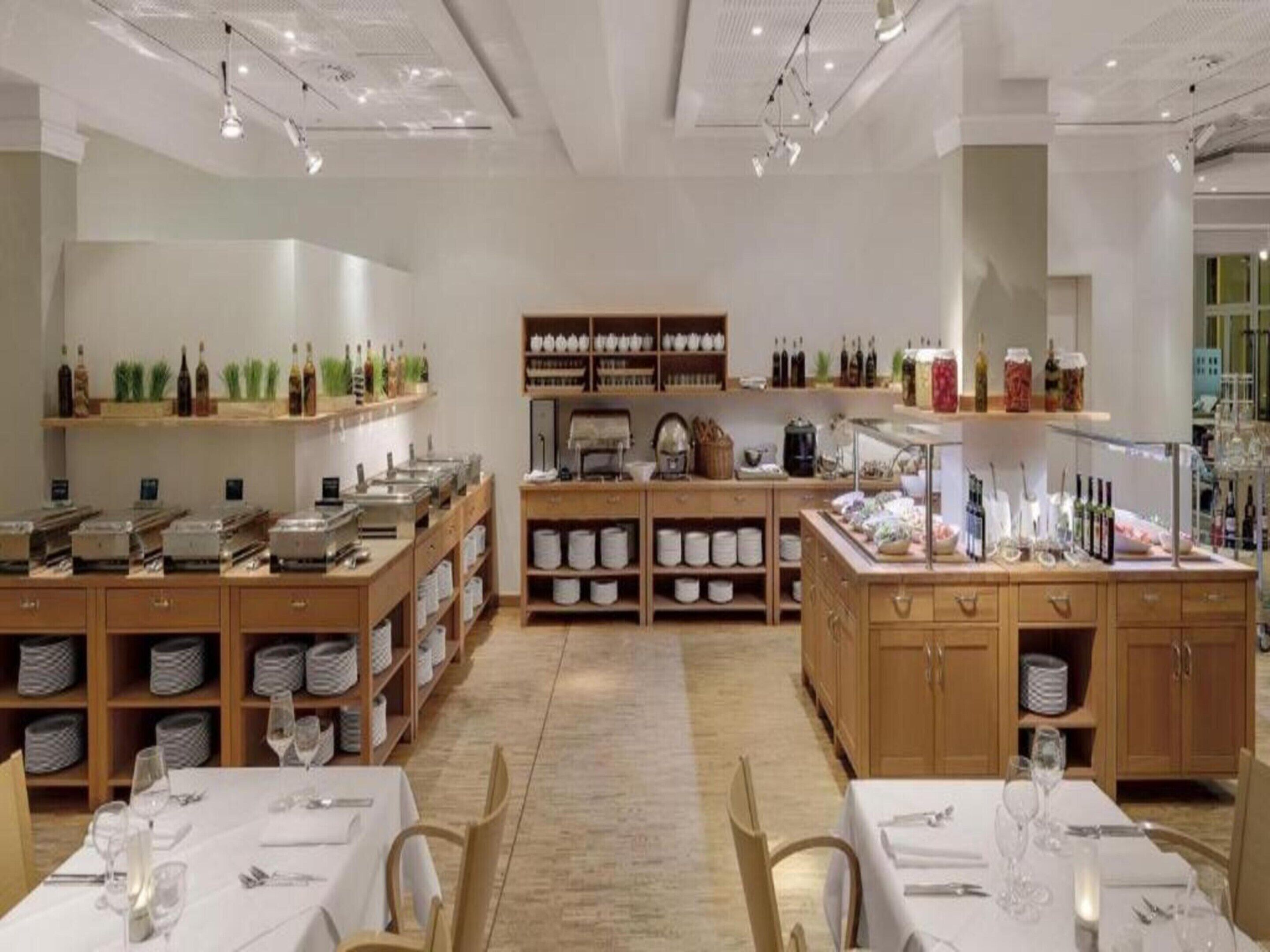 A restaurant with multiple dining tables, shelves with bottles and glasses, and a central counter with a coffee machine.