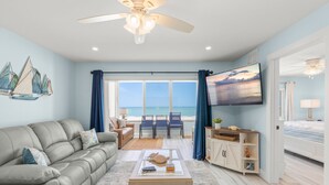 A living room with a sofa, coffee table, and TV, a balcony with chairs, and a view of the ocean. - Coastal Comfort with Gulf-Front Views (Sarasota)