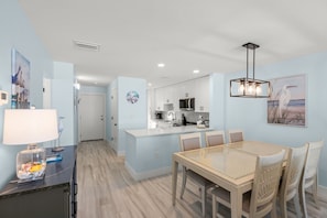 A modern kitchen with white cabinets, a central island, and a dining area with a glass table and chairs. - Coastal Comfort with Gulf-Front Views (Sarasota)