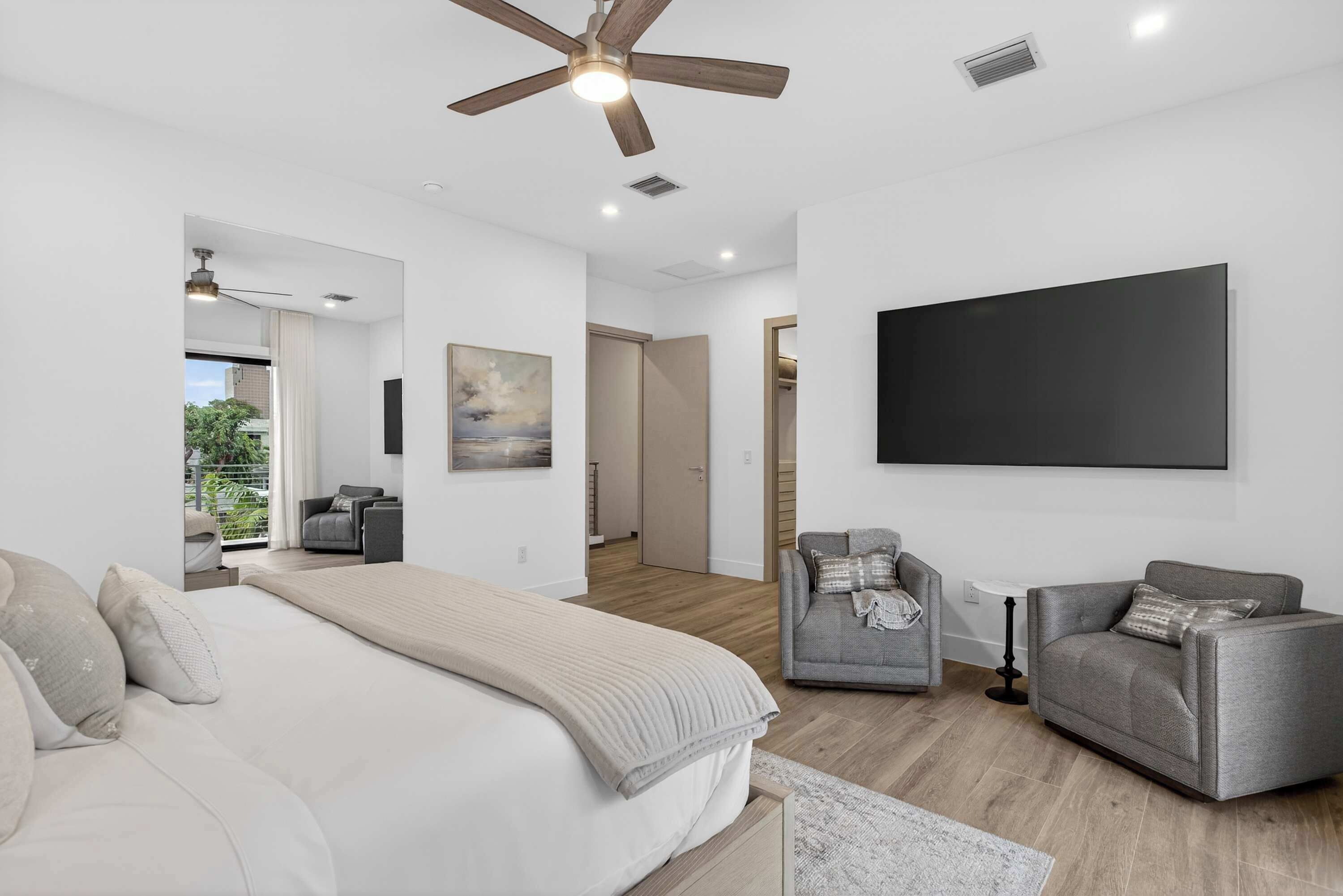 Une chambre moderne avec un grand lit, deux fauteuils, un ventilateur de plafond et un grand téléviseur.