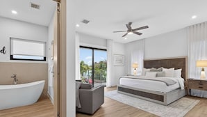 A modern bedroom with a large bed, a built-in bench, a ceiling fan, and a view of the outdoors. - Tarpon River Enclave - New Build (Fort Lauderdale)
