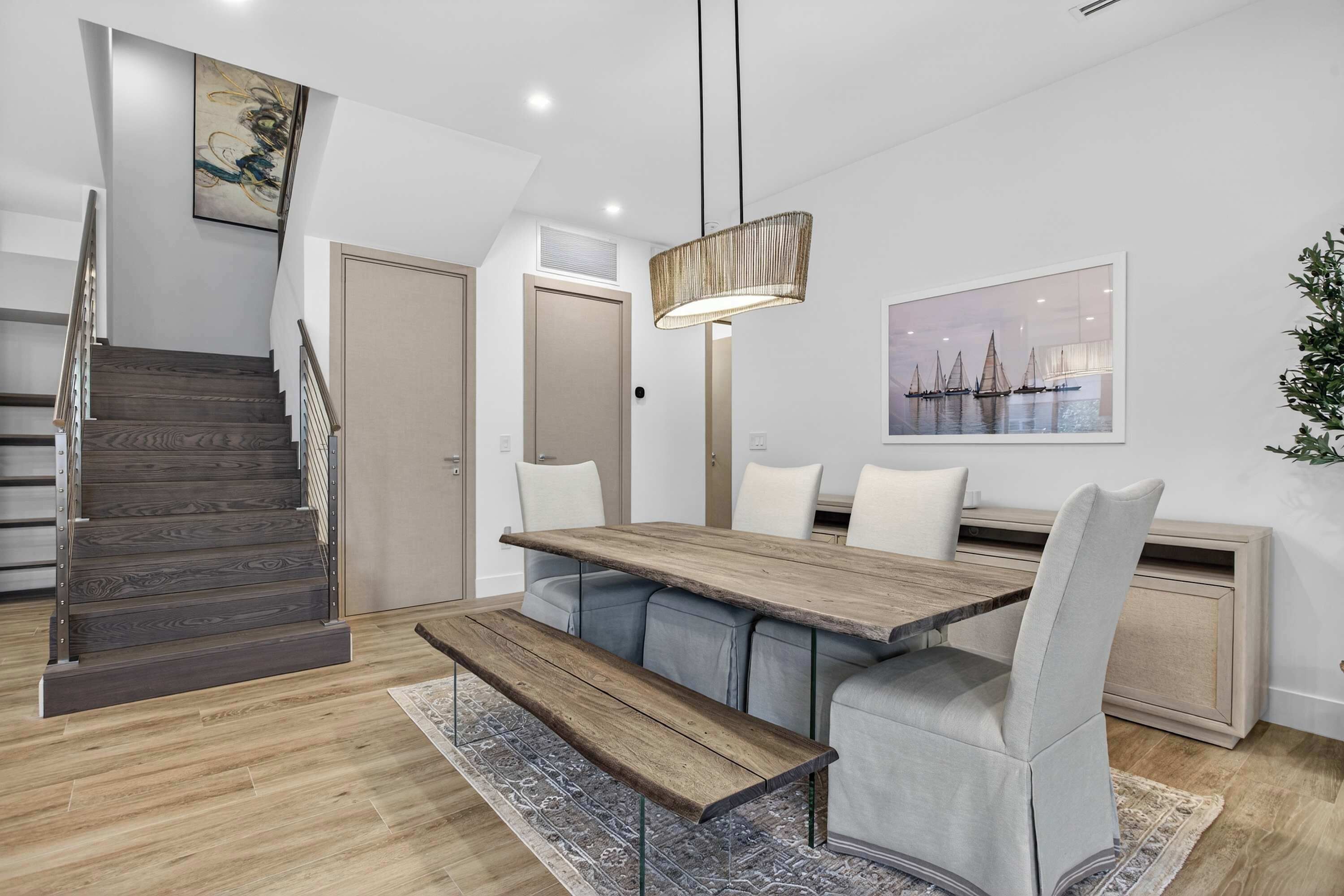 A modern dining area with a wooden table, bench seating, and a contemporary pendant light.