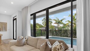 A modern living room with a beige sofa, large windows, and a view of a swimming pool. - Tarpon River Enclave - New Build (Fort Lauderdale)
