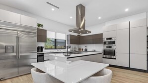 A modern kitchen with a central island, stainless steel appliances, and a large window providing natural light. - Tarpon River Enclave - New Build (Fort Lauderdale)