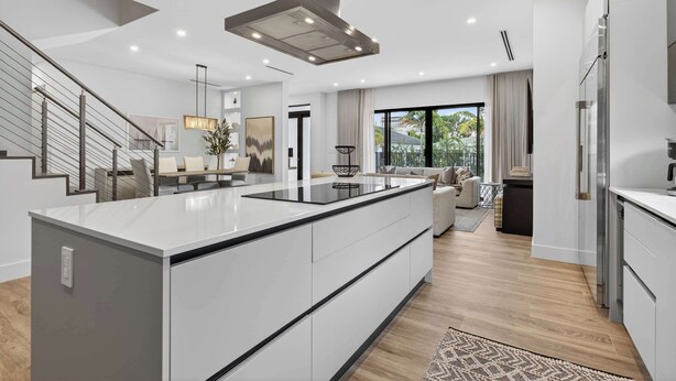A modern kitchen with a central island, a staircase, and a living area with a sofa and a large window. - Tarpon River Enclave - New Build (Fort Lauderdale)