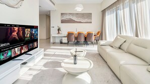 Ein modernes Wohnzimmer mit Flachbildfernseher, einer Couch, einem Essbereich mit Stühlen und einem großen Fenster mit Vorhängen.