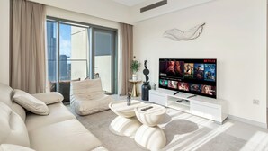 Ein modernes Wohnzimmer mit einem großen Flachbildfernseher, der Netflix-Inhalte zeigt, einem beigen Sofa, einem Couchtisch und Blick auf die Stadt durch ein großes Fenster.