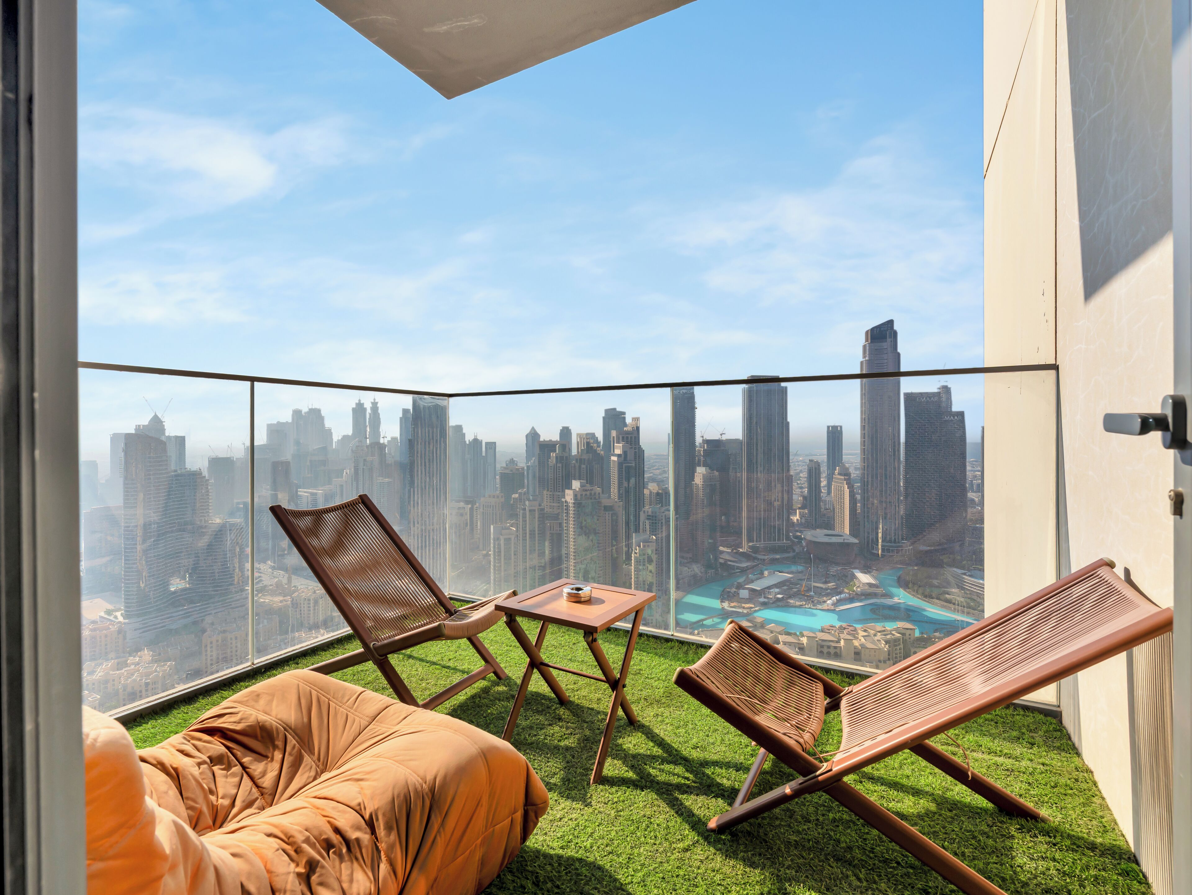 A balcony with a city view, two lounge chairs, a small table, and artificial grass flooring.
