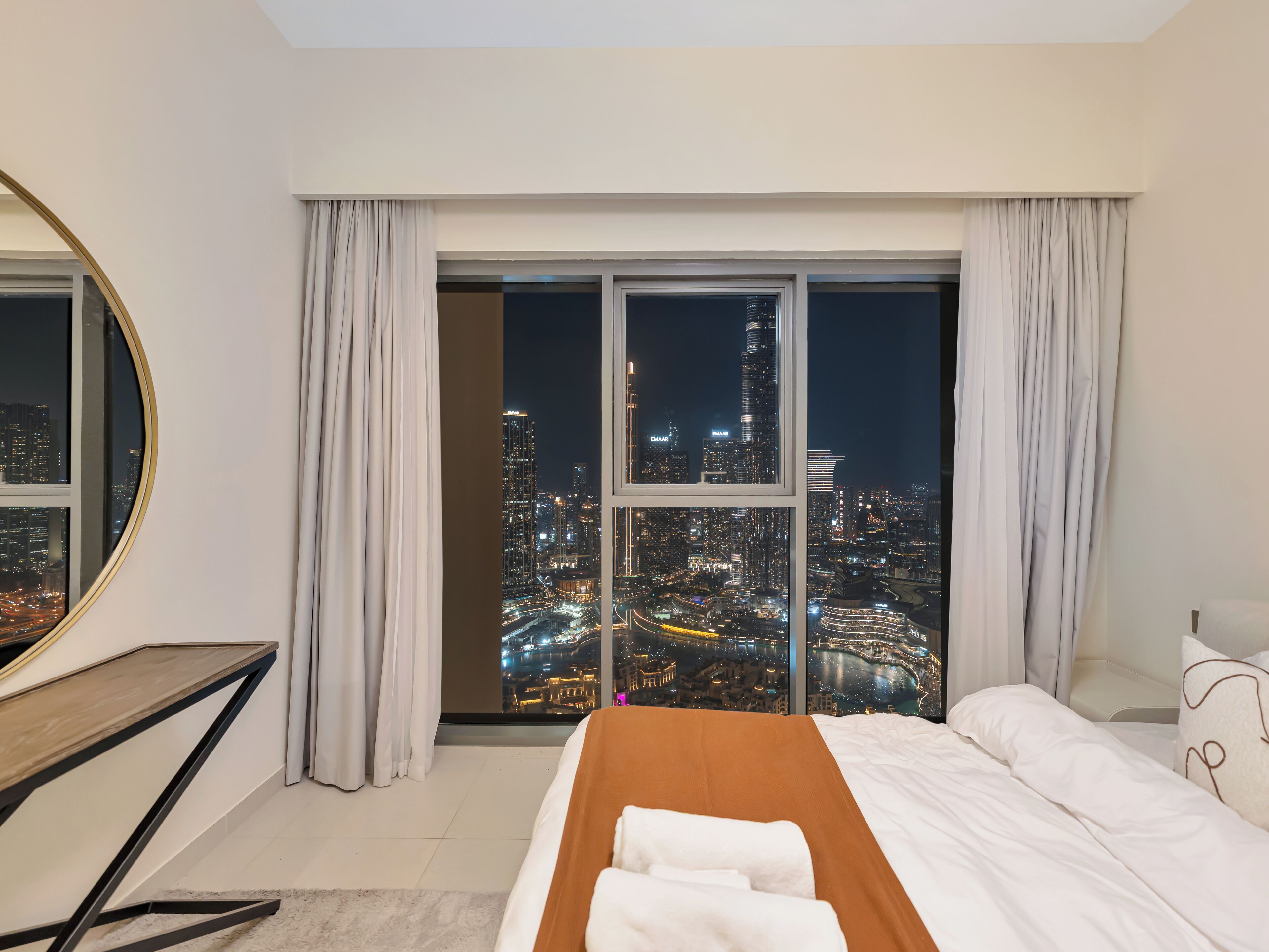 A hotel room with a large bed, a desk, and a view of a cityscape at night.