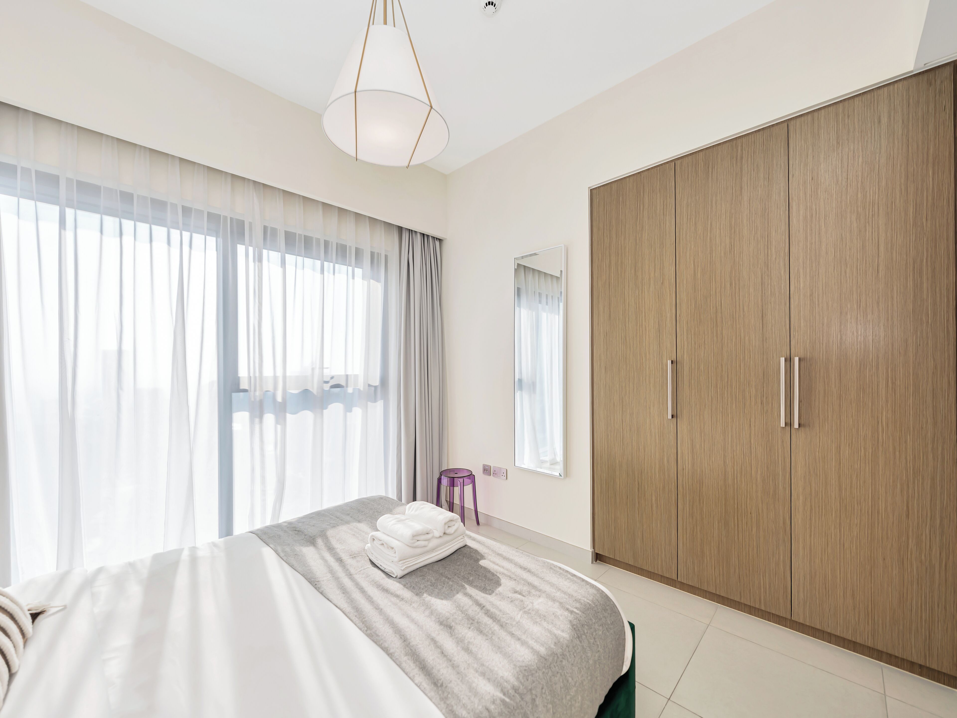 Un dormitorio moderno con una cama grande, un armario y una ventana con cortinas translúcidas.