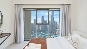 Ein Hotelzimmer mit einem großen Bett, einem Schreibtisch und Blick auf eine Stadtlandschaft durch raumhohe Fenster.