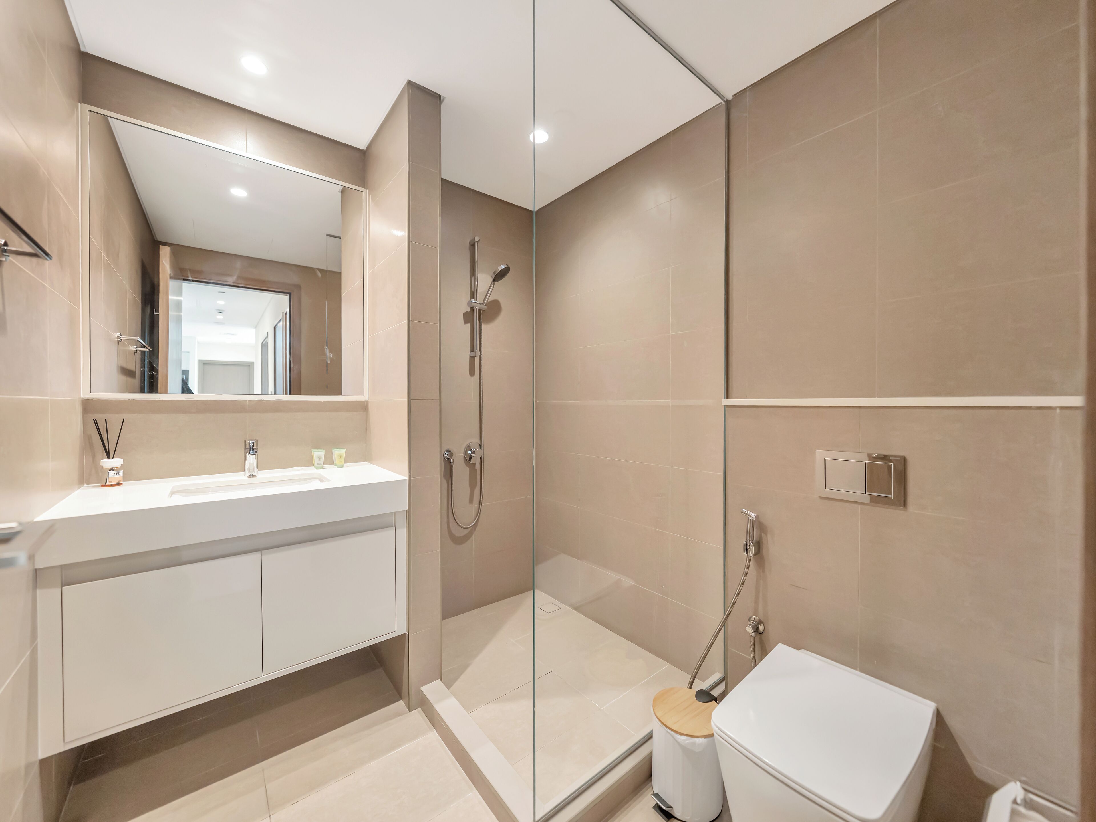 Un baño moderno con ducha de vidrio, un lavamanos blanco con espejo y un inodoro.