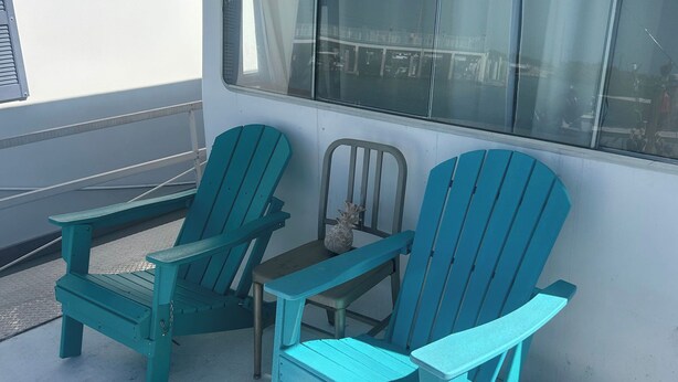 Deux chaises Adirondack turquoise et une petite table sont placées sur un patio en béton, à côté d’un bâtiment doté de grandes fenêtres.