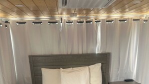 Une chambre à coucher avec un lit, des rideaux blancs, une tête de lit en bois et une table de chevet avec une télécommande.