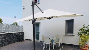Un patio con una sombrilla blanca, una mesa con sillas y una planta en maceta.