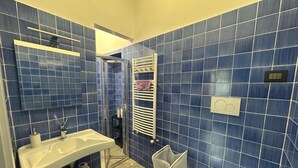 Un baño con azulejos azules, un lavamanos blanco, un inodoro y una zona de ducha.