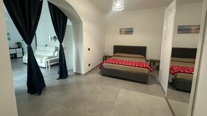 Un dormitorio moderno con una cama grande, una mesita de noche, una lámpara colgante y vistas a una sala de estar con un sofá y cortinas.