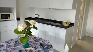 Une cuisine de taille réduite avec des meubles blancs, un plan de travail noir, un four à micro-ondes et un vase de fleurs posé sur une table.