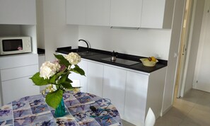 A compact kitchen with white cabinets, a black countertop, a microwave, and a vase with flowers on a table. - Flat on the Shores of Lignano (Lignano Sabbiadoro)