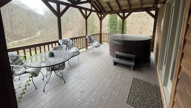 Eine überdachte Terrasse im Freien mit Whirlpool, Metallstühlen und einem Tisch.