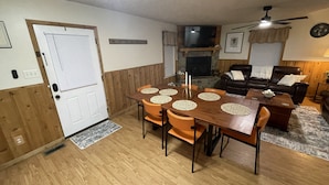 Ein Essbereich mit Holztisch und -stühlen, einem Kamin, einem Ledersofa und einer Wanduhr.