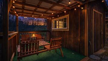 Una terraza de madera con una mesa y sillas, rodeada por una valla de madera y una pérgola con luces colgantes.