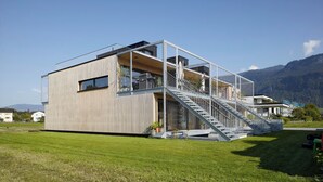 Un edificio moderno con un amplio muro de cristal, una escalera que conduce a un nivel superior y vistas de montañas al fondo.