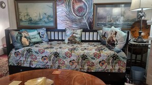 Un dormitorio con una cama grande, varios almohadones, una mesita de madera y dos cuadros en la pared.