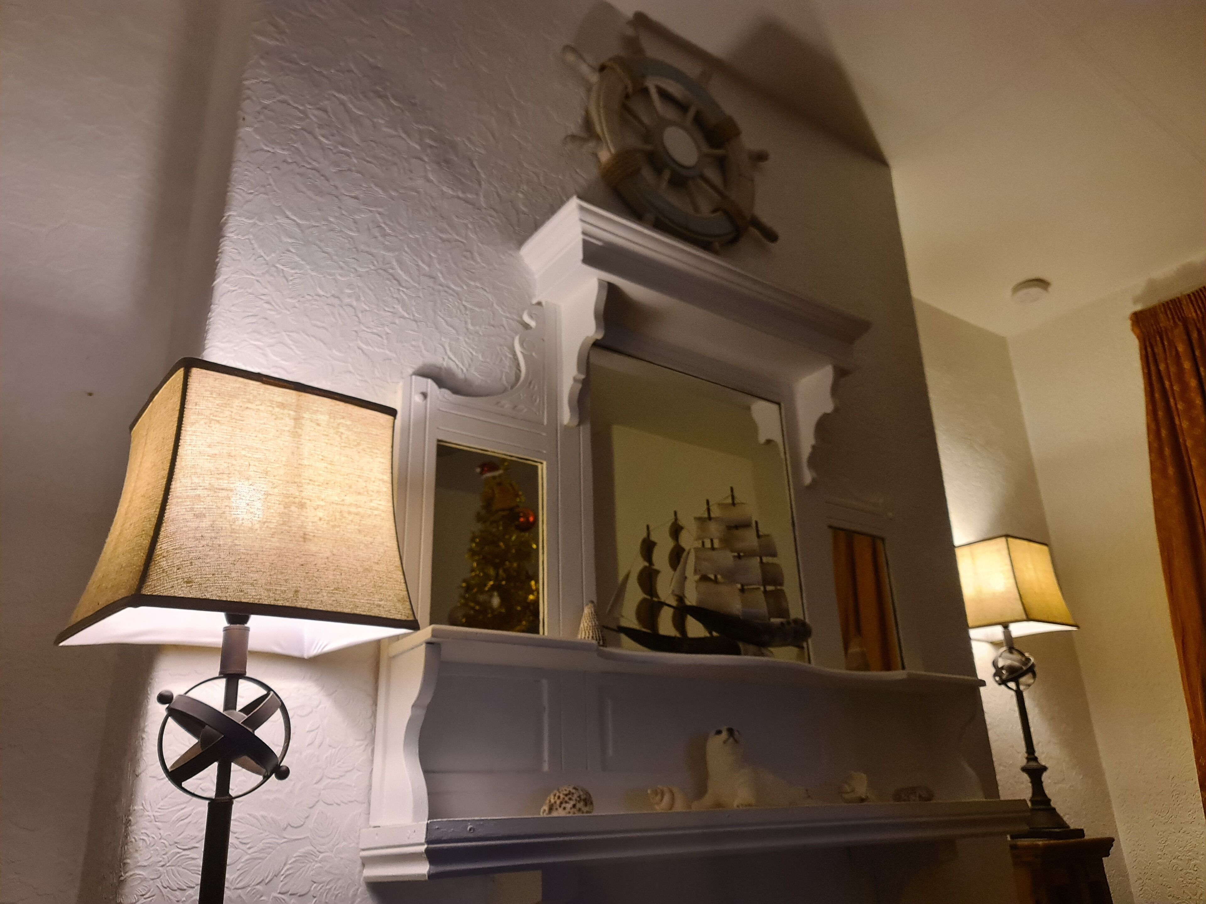 A fireplace with a ship model, a ship wheel decoration, and a Christmas tree.