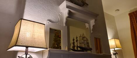 A fireplace with a ship model, a ship wheel decoration, and a Christmas tree.
