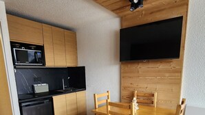 Cocina compacta con armarios de madera, un microondas y una mesa de comedor con sillas.