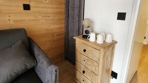 Una habitación con pared de madera, un sofá gris, un aparador de madera con tazas y una lámpara fijada a la pared.
