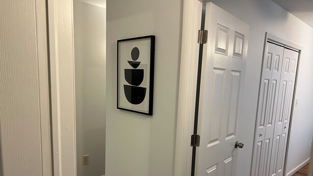 A hallway with white walls, a framed abstract artwork, and a set of white doors with a classic design. - Cozy 3BR Apartment in Peaceful Neighborhood With Kitchenette (Commack)