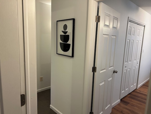 A hallway with white walls, a framed abstract artwork, and a set of white doors with a classic design.