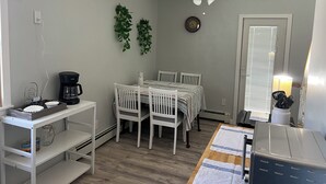 A compact kitchen with white cabinetry, a coffee maker, a dining table with chairs, a ceiling fan, and a clock on the wall. - Cozy 3BR Apartment in Peaceful Neighborhood With Kitchenette (Commack)