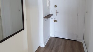 En gang med hvid dør, hvid radiator, hvid pendellampe og en hvid vægmonteret hylde.