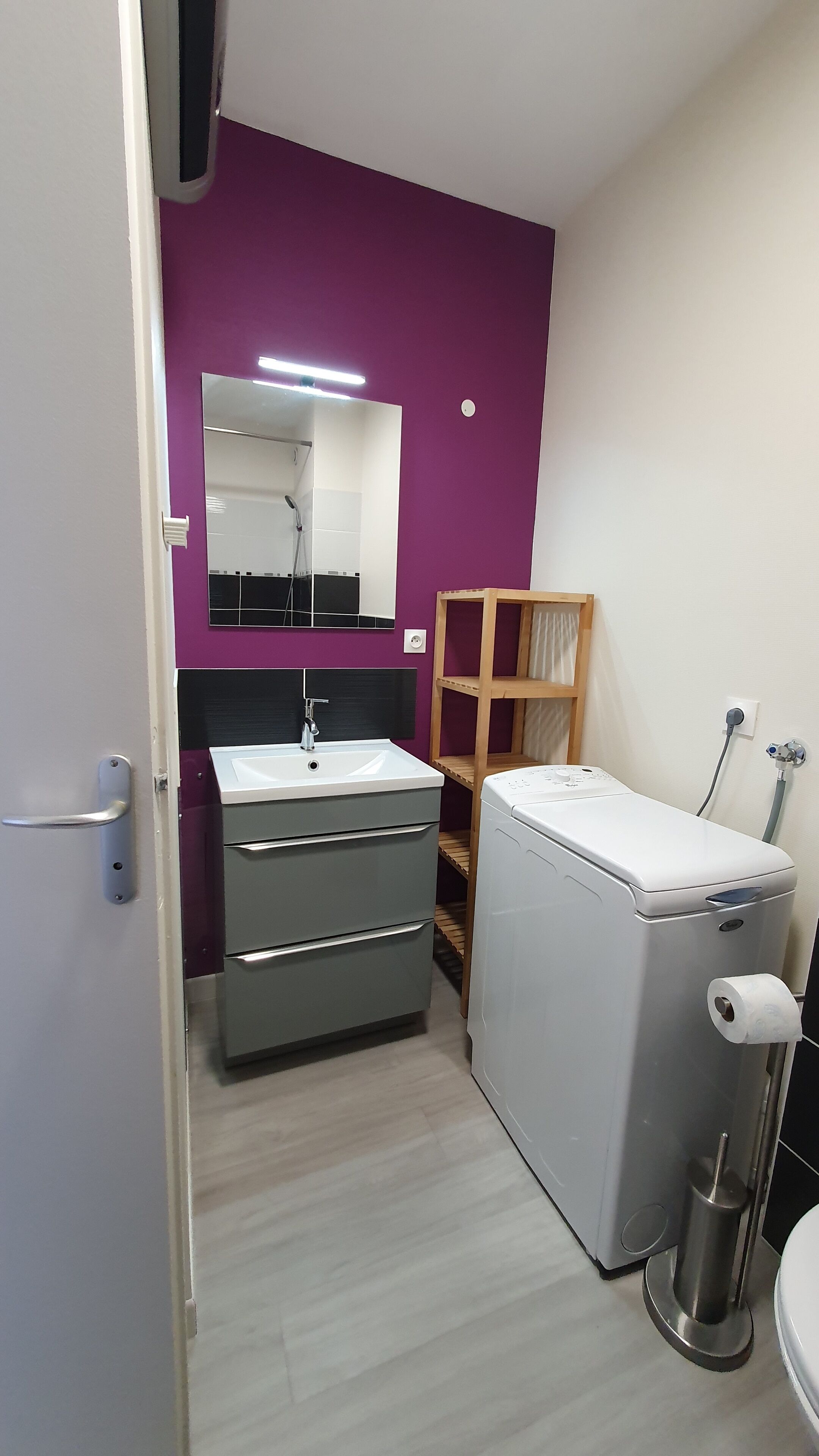 Un bany petit i pràctic amb un lavabo modern, un mirall, una rentadora integrada i una prateleira de fusta.