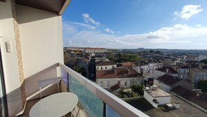 En balkon med et bord og stole, udsigt over et bybillede med historiske bygninger og en klar himmel.
