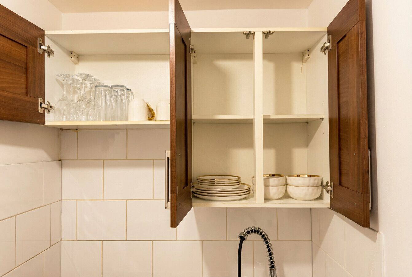 Een keuken met open houten kastjes, een betegelde spatwand en een kraan.