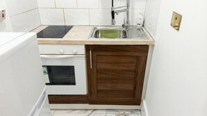 Eine kleine Küche mit weißen Geräten, einem Spülbecken und einem Holzkasten.