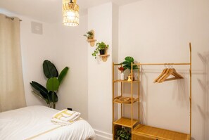 Un dormitorio con una cama, un perchero, una estantería con plantas y una lámpara colgante.