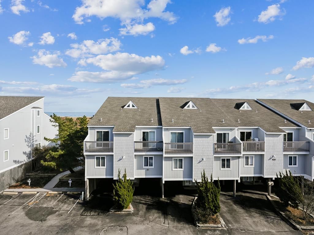 A multi-story residential building with balconies, a parking lot, and a clear sky.